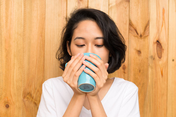 Asiática joven desayunando sosteniendo una taza de café
 - Foto, Imagen