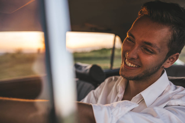 Closeup portrait of handsome happy male driver smiling while sitting in a car with open front window looking to the road during road trip. Caucasian businessman drive a car with toothy healthy smile. - Фото, изображение