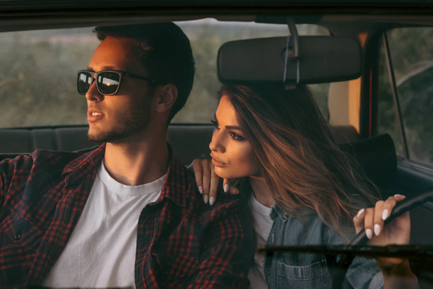 Attractive portrait of romantic young couple going on a long drive in car on sunset light. Handsome young man wearing sunglasses with his beautiful girlfriend on a road trip. Lifestyle concept. - Foto, afbeelding
