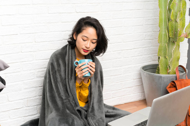 Asian young woman sitting on the floor holding a cup of coffee - Photo, Image