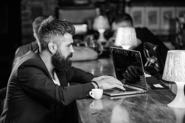 Coffee break concept. Man bearded businessman sit bar counter with laptop and cup of coffee. Create content web blog. Manager create post enjoy coffee. Hipster freelancer work online drinking coffee - Photo, Image