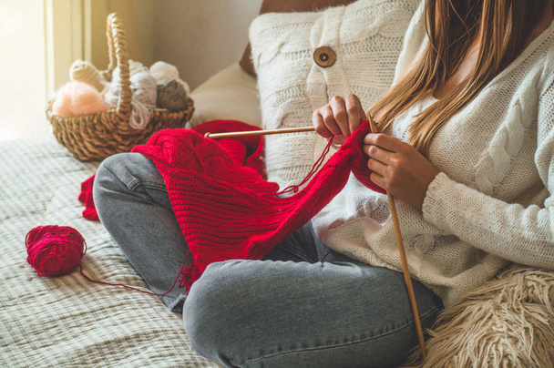 Mooi meisje knits een warme trui op het bed. Accessoires voor breien. - Foto, afbeelding