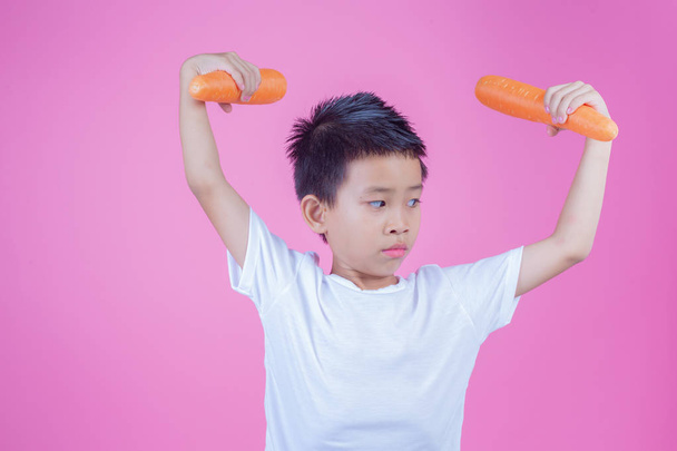 Boy holding a carrot on a pink background. - Φωτογραφία, εικόνα