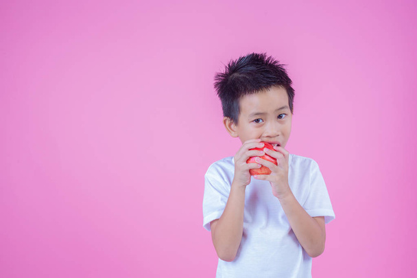 Boy holds and eats red apples on a pink background. - Foto, Imagem