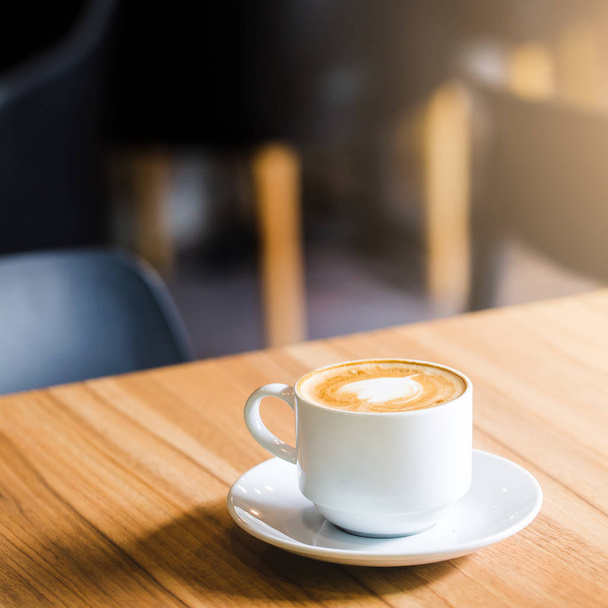 Latte káva v šálku na dřevěném stole a rozmazání v kavárně - Fotografie, Obrázek