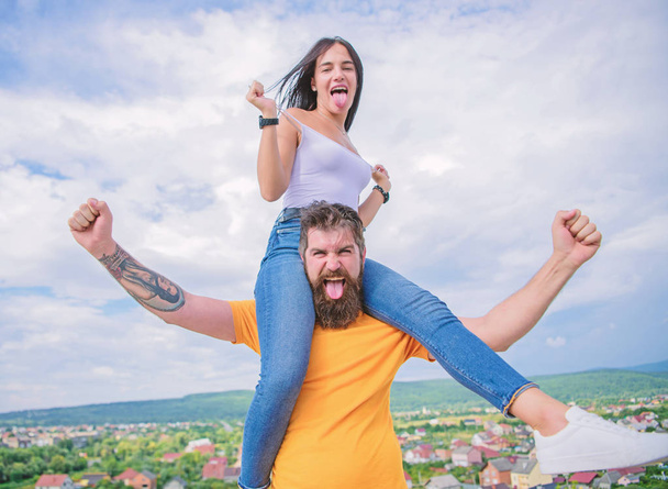 Having some chemistry. Hipster giving sexy woman a piggyback ride. Happy couple in love on cloudy sky. Loving couple happy smile having fun. Bearded man piggybacking his girlfriend just for fun - Photo, image