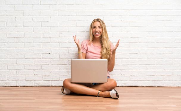 Young blonde student girl with a laptop on the floor unhappy and frustrated with something - Photo, Image