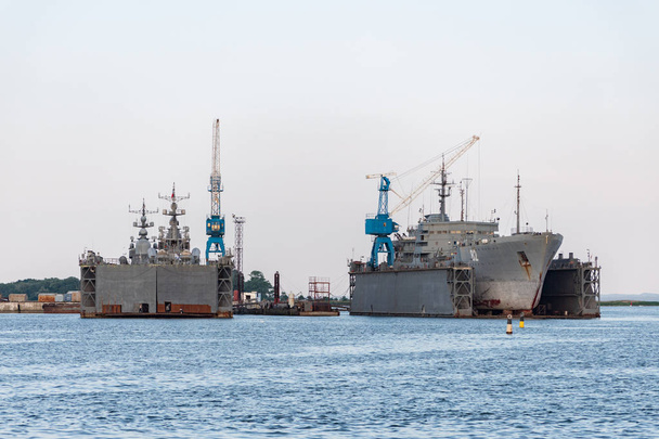 修理のための造船所で大型鉄海軍艦艇。ドックヤードの大きなクレーン。青い海の港 - 写真・画像