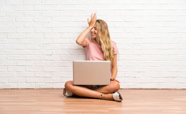 Jovem estudante loira com um laptop no chão com dúvidas com expressão facial confusa
 - Foto, Imagem