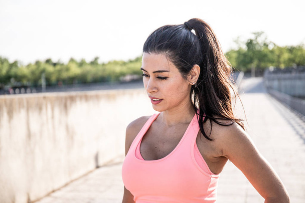 Latin woman with ponytail in her hair gets ready to go for a run. Dress a pink body - Фото, зображення