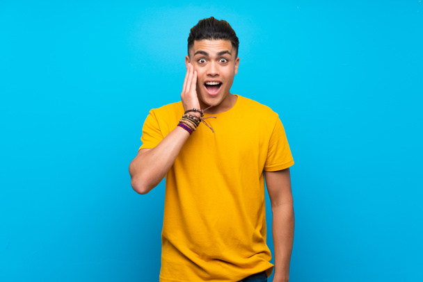 Giovane uomo con camicia gialla su sfondo blu isolato con sorpresa e espressione facciale scioccata
 - Foto, immagini