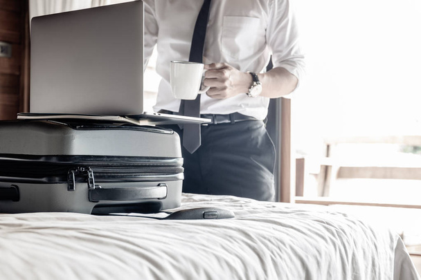 Biznesmen Stoiska i przechowywania kawy i pracy na laptopie w pokoju hotelowym podczas podróży służbowej. - Zdjęcie, obraz