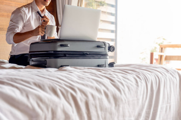 Businessman holding coffee cup with open laptop on suitcase in bed. - Foto, immagini