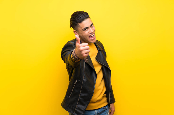 Young man over isolated yellow background with thumbs up because something good has happened - Valokuva, kuva