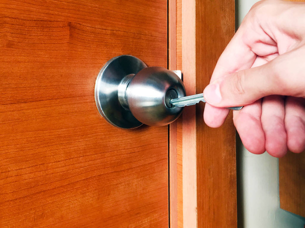 De sleutel wordt in het deurslot gestoken. De sleutel is in de mannelijke hand. Metalen slot op houten deur. Close-up. - Foto, afbeelding