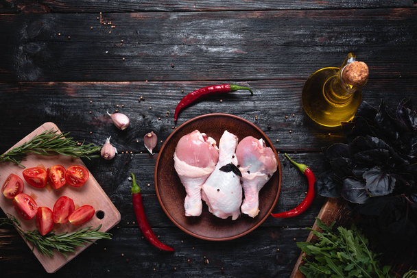 pernas de frango crus jazem na mesa, temperos perfumados alho, pimenta e manjericão. Ingredientes para fazer carne deliciosa
. - Foto, Imagem