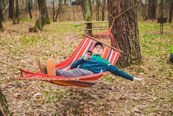 young man laying in hammock surfing in phone - Photo, Image
