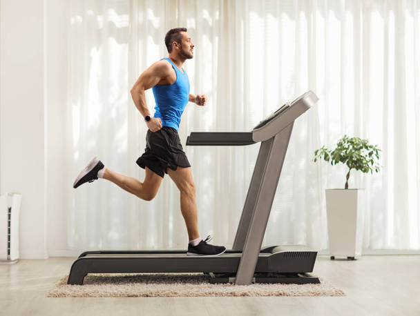 Young man running on a treadmill at home  - Фото, изображение
