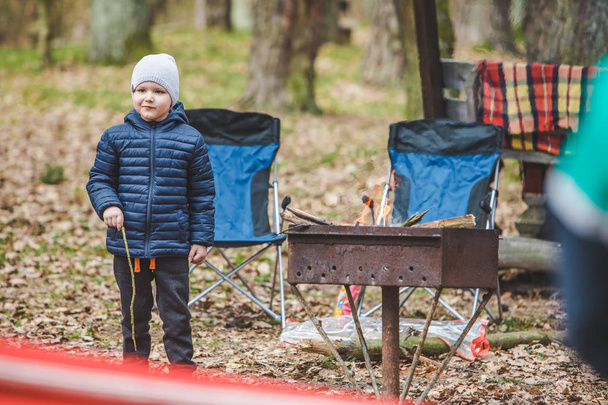 Мальчик играет на свежем воздухе в кемпинге. огонь на гриле для приготовления пищи
 - Фото, изображение