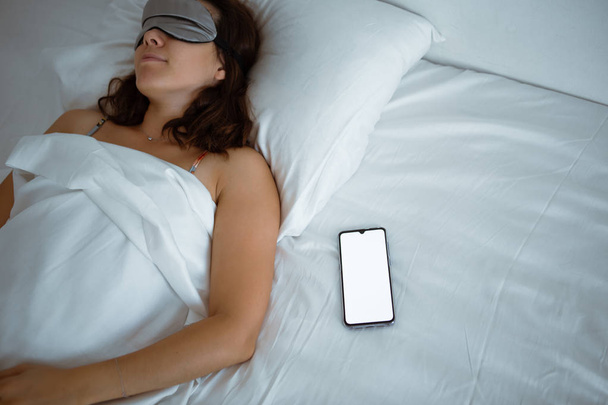 彼女の近くに睡眠マスクスマートフォンで眠っている女性 - 写真・画像