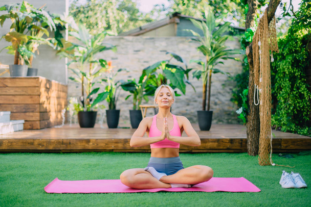 Mujer joven se sienta en posición de loto sobre hierba verde, concepto de yoga y meditación
. - Foto, Imagen