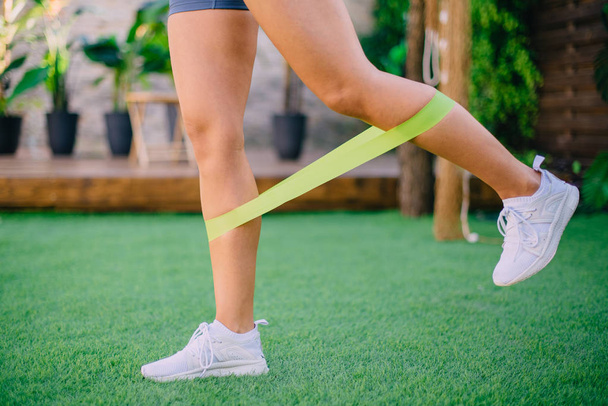 Close up woman is exercising with resistant band on lawn - Photo, Image