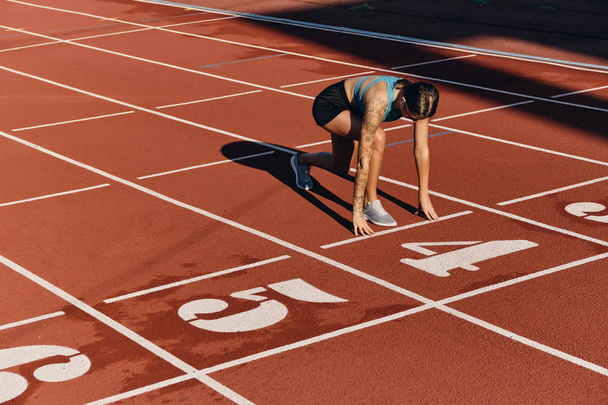 Pewna dziewczyna sportowiec w odzieży sportowej stojącej w pozycji wyjściowej gotowy do biegania na stadionie miejskim - Zdjęcie, obraz