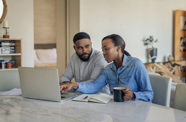 Young African American couple sitting together at their dining room table at home going over bills and doing online banking - Foto, Bild