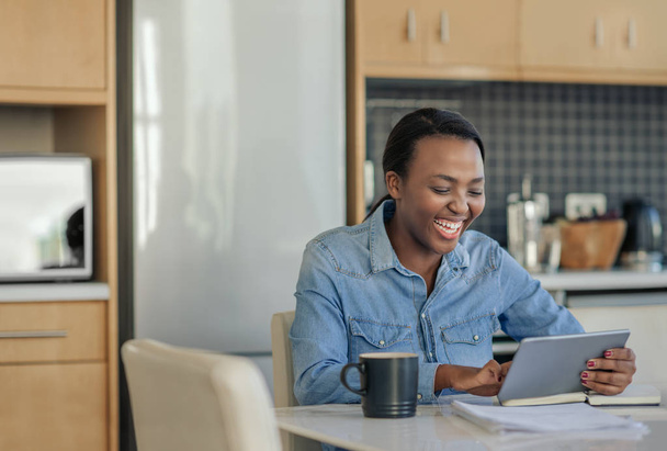 Young African american woman laughing while working at her kitchen table at home with a digital tablet - Фото, зображення