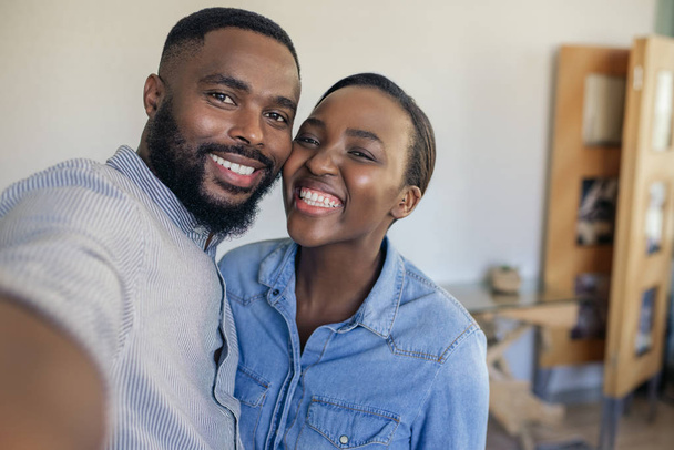Χαμογελαστός νέος Αφρικανός Αμερικανός ζευγάρι στέκεται στο σαλόνι τους στο σπίτι παίρνοντας μια selfie μαζί - Φωτογραφία, εικόνα