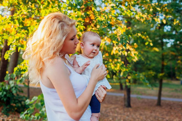 Die junge Mutter geht mit ihrem Baby im Sommerpark spazieren. glückliche Frau mit Kind im Freien. Mutter umarmt Tochter - Foto, Bild