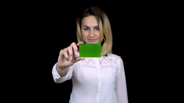 Een jonge zakenvrouw in een wit shirt heeft een bankkaart in haar hand. Geïsoleerde zwarte achtergrond. Chromakey groene kaart. 4k - Video