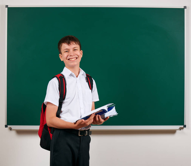 Portret chłopca szkolnego stwarzające z plecaka i materiałów szkolnych, tablica tła-powrót do szkoły i koncepcji edukacji - Zdjęcie, obraz
