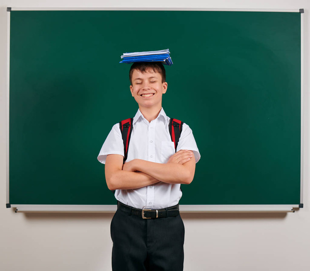 Portré egy iskolás fiú pózol a hátizsák és az iskolai kellékek, tábla háttér-vissza az iskolába és az oktatás koncepció - Fotó, kép