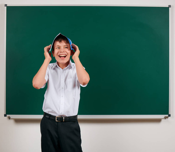 Портрет школьника, позирующего с синей тетрадью на фоне доски - возвращение к школьной и образовательной концепции
 - Фото, изображение