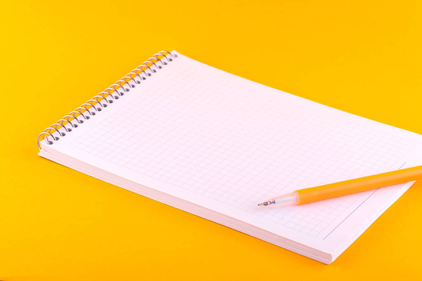 Ноутбук на пружине с белыми листами бумаги для рисунков, текстов и заметок, рядом с желтой ручкой лежит на оранжевом фоне
 - Фото, изображение