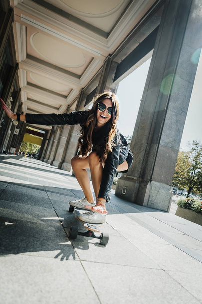 街で彼女の長いボードに乗って美しい若いスケーターの女性。ストリートウェアのスタイリッシュな女の子は、ロングボードに乗ります。スケートボード、ストリートフォト、ライフスタイル、自由、ハッピーフェイスコンセプト. - 写真・画像