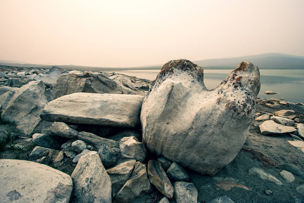 D'énormes rochers au premier plan dans la steppe au bord du lac par un matin brumeux. Grandes pierres entassées en tas. Teintée. Espace de copie
. - Photo, image