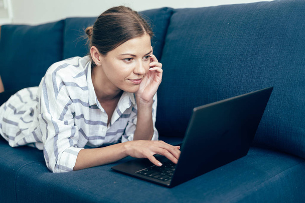 Young adult woman lying on sofa, using laptop - Foto, Imagen