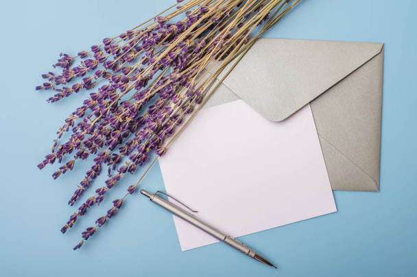 Lavender flowers and blank paper with an envelope on a blue background. View from above. mock up - Φωτογραφία, εικόνα