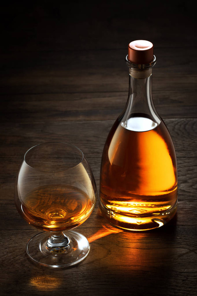 θέα από το ποτήρι του κονιάκ και ένα μπουκάλι στην άκρη σε χρώμα ξύλινο φόντο.  - Φωτογραφία, εικόνα