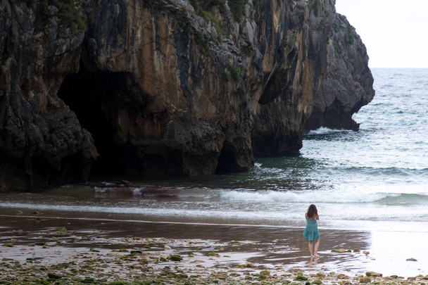 Samotna dziewczyna spaceru w plaży z klifem w tle. Lokalizacja plaża jaskinie morskie w Asturii, Hiszpania. - Zdjęcie, obraz