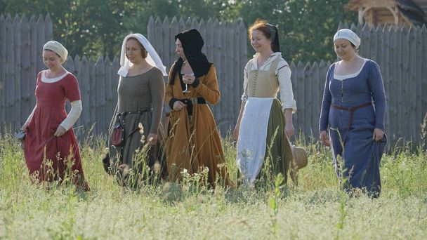 Mittelalterliche Frauen, die vor hölzernem Festungshintergrund vor der Kamera stehen. Kleidung mittelalterlicher Frauen aus dem 14. bis 15. Jahrhundert. - Foto, Bild