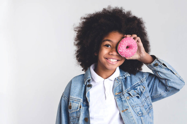 Une fille à la peau foncée tient un beignet près de son œil et sourit
. - Photo, image