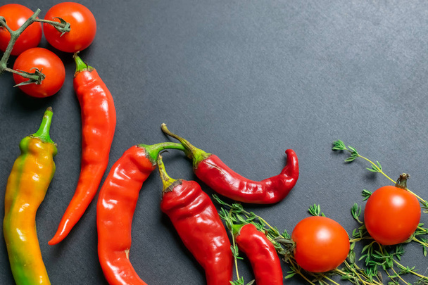 frische Chilischoten mit Tomaten und Thymian, Wurst- oder Salatzutaten auf schwarzem Schieferbrett - Foto, Bild