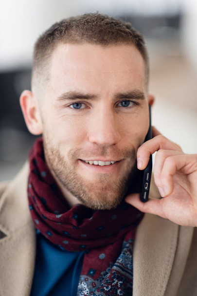 Young serious man wearing scarf and coat talking on mobile phone close-up. - Fotoğraf, Görsel