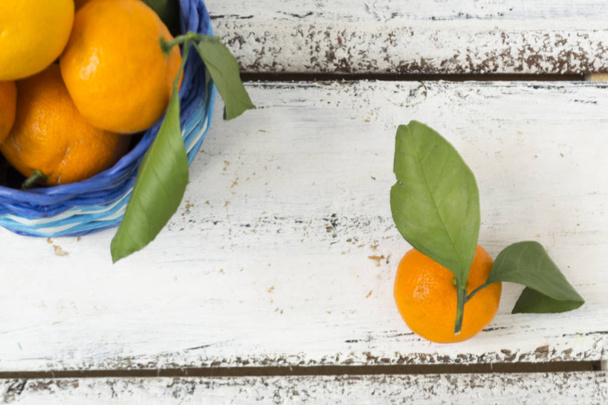 Tangerines pomarańcze, klementynki, owoce cytrusowe, z zielonymi liśćmi leżą w wiklinowym koszyku na drewnianym tle z kopią przestrzeni. Widok z góry. - Zdjęcie, obraz