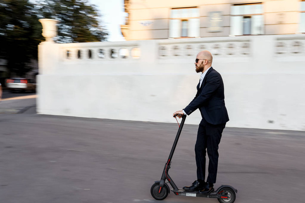Attractive business man riding a kick scooter at cityscape background - Foto, imagen