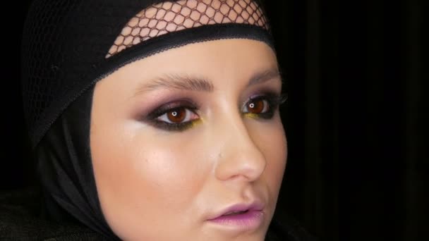 Profesionální dívčí model s nádherným make-upem představuje v černé čepici na hlavě před kamerou na černém pozadí v obraze černé vdovy. High-móda - Záběry, video