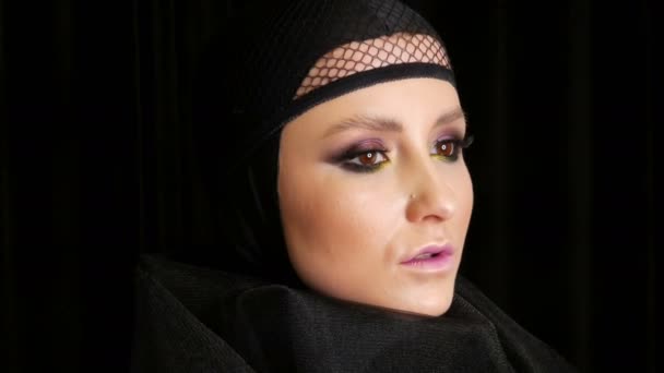 Profi-Model mit wunderschönem Make-up posiert in einer schwarzen Mütze auf dem Kopf vor der Kamera auf schwarzem Hintergrund in dem Bild einer schwarzen Witwe. Mode im Trend - Filmmaterial, Video